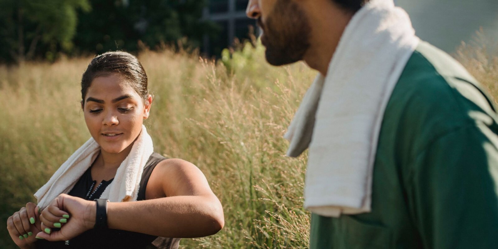 A couple outdoors using fitness trackers after a workout, wearing towels.